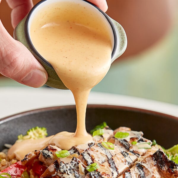 A person pouring Terry Ho's Original Yum Yum Sauce over a bowl of food.