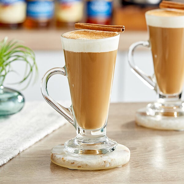 A glass mug of brown pumpkin spice liquid with a cinnamon stick in it.