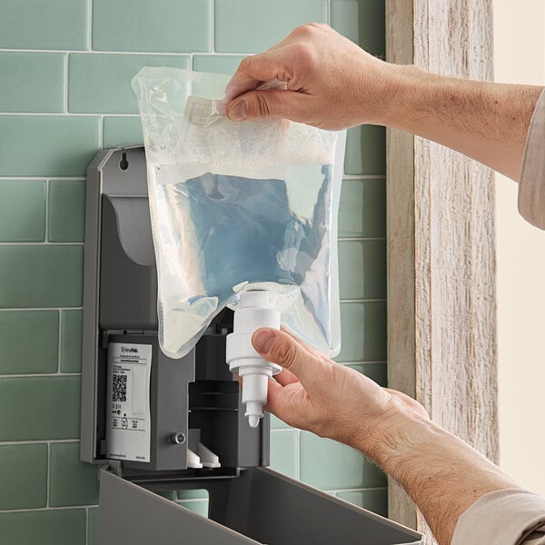 A hand using a Lavex bag of foaming hand sanitizer to refill a dispenser.