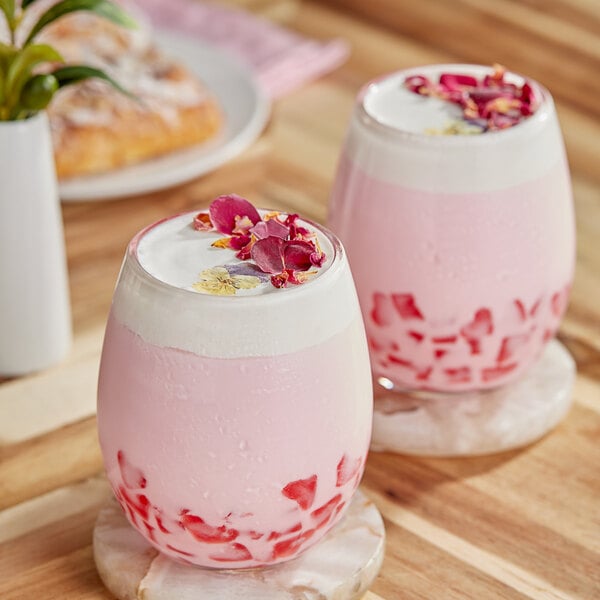 Two glasses of pink and white layered Fanale Sakura drinks with flowers on top.