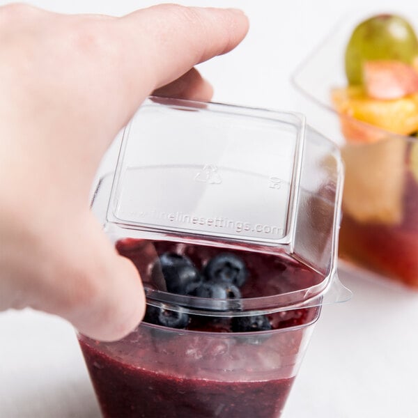 A hand holding a plastic container of fruit with a clear plastic lid.