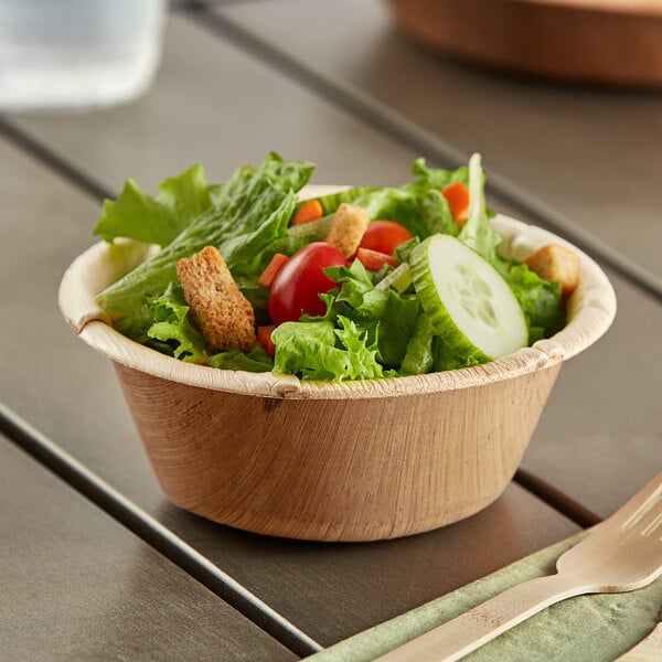 A wooden spoon in a bowl of salad on a table.