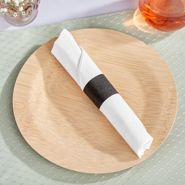 A wooden plate with a white Choice 1/4 fold dinner napkin and a black self-adhering paper napkin band.