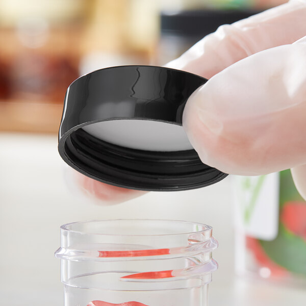 A person in gloves holding a plastic container with a black 33/400 plastic lid.