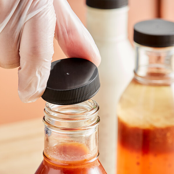 A hand wearing a white glove holding a plastic bottle with a black lid.