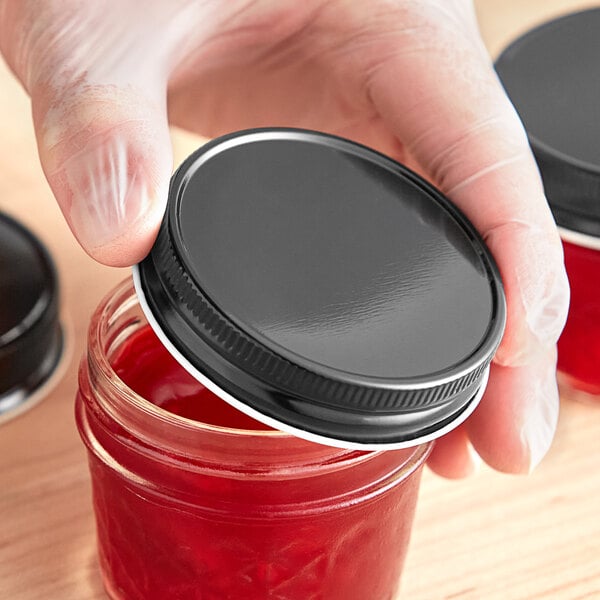 A person holding a jar of red liquid with a 70/450 black metal lid.