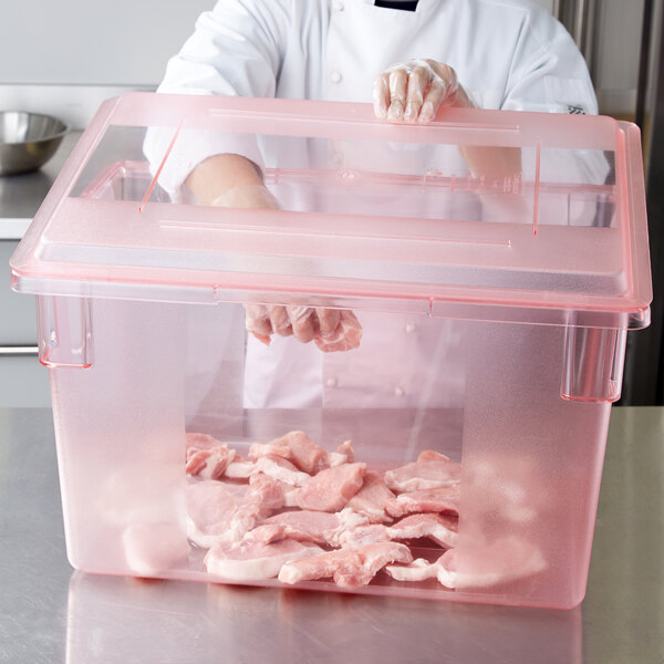 A person in a white shirt and gloves holding a Carlisle red plastic food storage container with raw meat in it.