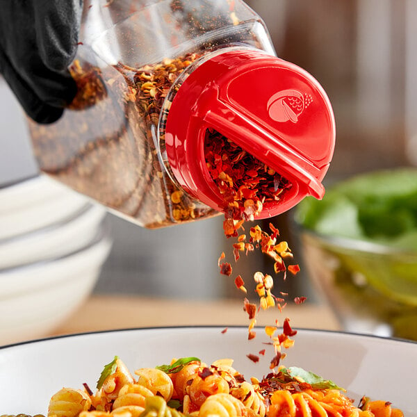 A person sprinkling red pepper flakes on a bowl of food.