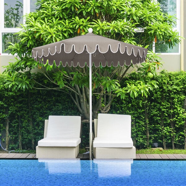 A white patio umbrella with a scalloped edge over two chairs.