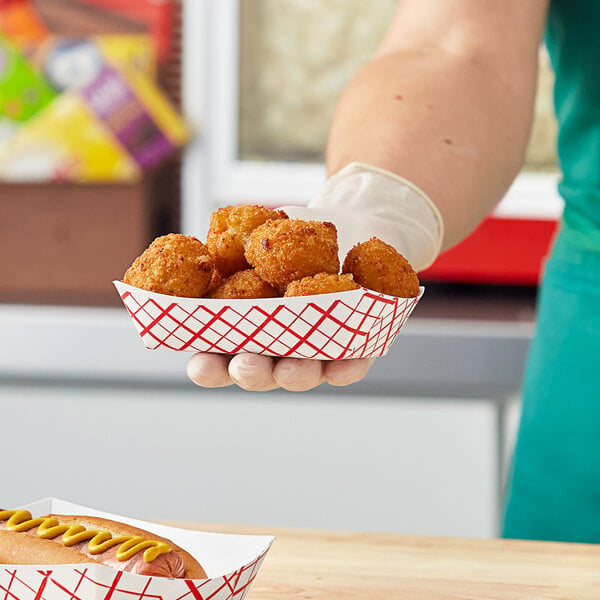 A hand holding a red checkered paper food tray of fried food.