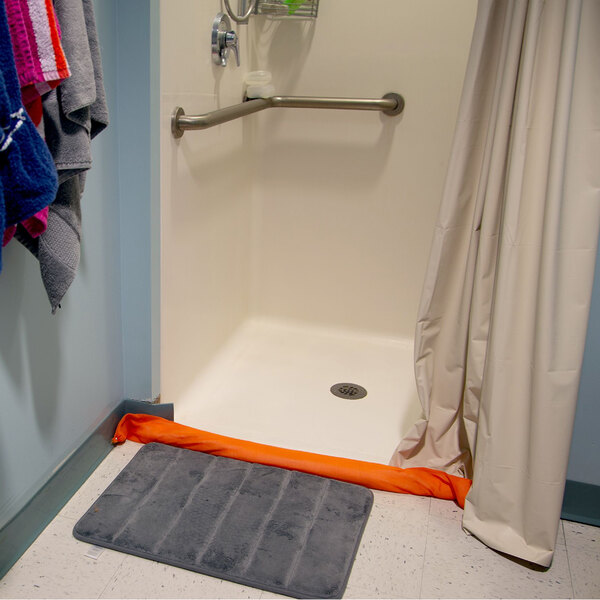 Quick Dam 4' Hi-Vis Orange Water Dam in a shower with a towel on the floor.