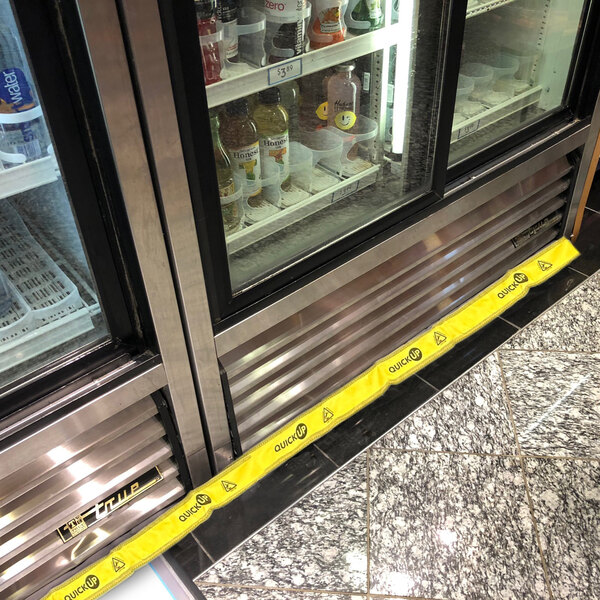 A Quick Dam yellow water dam on the floor in front of a refrigerator with drinks in it.