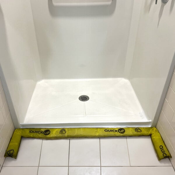 Quick Dam yellow water barrier tape on a white surface over a drain.