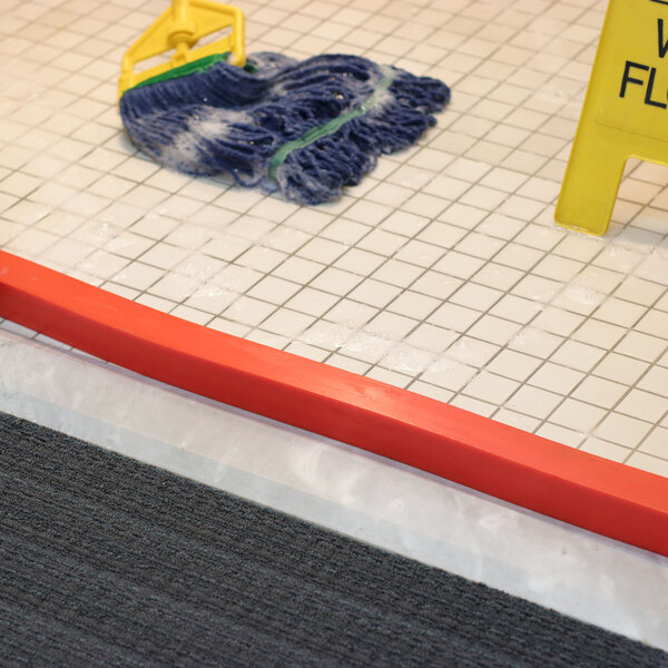 A Quick Dam Hi-Vis orange flood barrier with a yellow sign on the floor.
