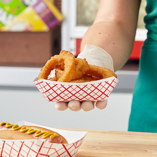 A hand holding a Southern Champion red checkered paper food tray with fried food.