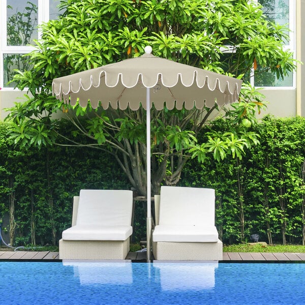 A white patio table with two chairs under a 7.5ft patio umbrella with a scalloped edge.