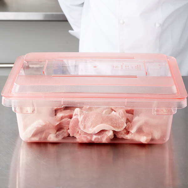 A chef wearing a white coat holding a Carlisle red plastic lid over a container of raw meat.