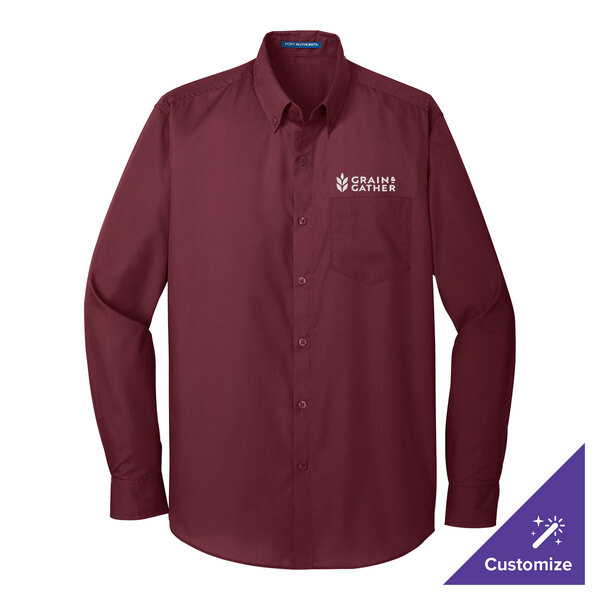 A Port Authority long sleeve maroon dress shirt on a counter with the word "school" embroidered on it.