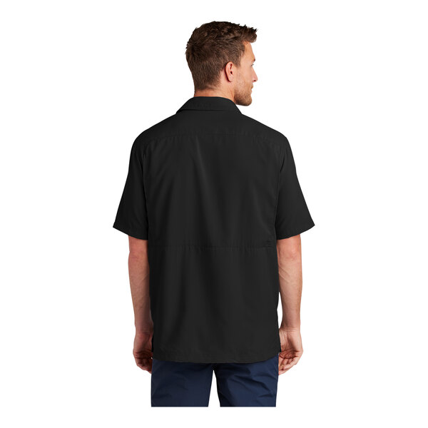 A man wearing a black Port Authority short sleeve shirt.