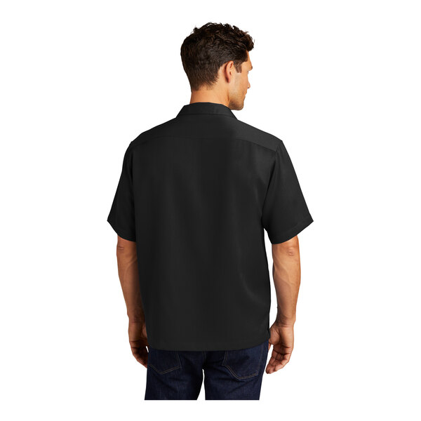 A man wearing a black Port Authority short sleeve camp shirt.