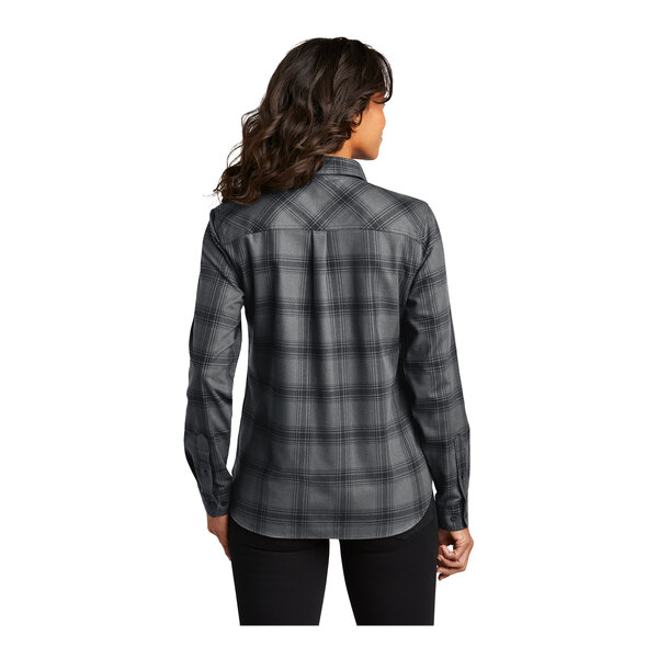 A woman wearing a Port Authority long sleeve flannel plaid shirt with a gray and black open plaid pattern.