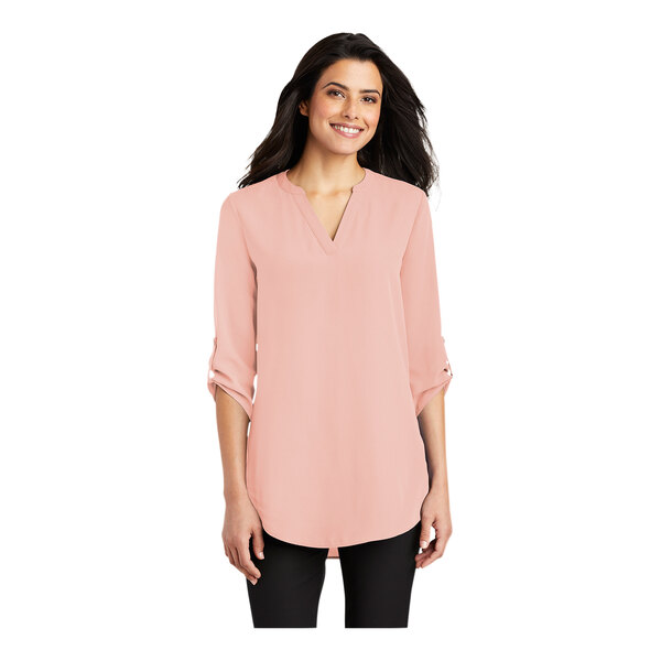 A woman wearing a rose quartz Port Authority short sleeve blouse.