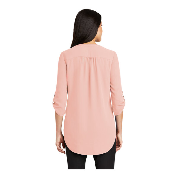 A woman wearing a rose quartz Port Authority short sleeve blouse.