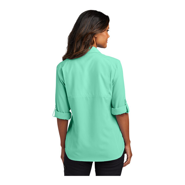A woman wearing a bright seafoam short sleeve Port Authority shirt.