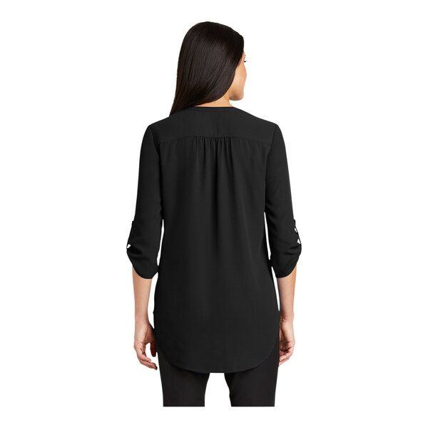 A woman wearing a black short sleeve Port Authority blouse.
