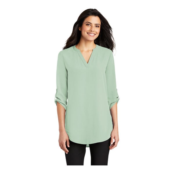 A woman wearing a misty sage Port Authority short sleeve blouse with a v-neck.