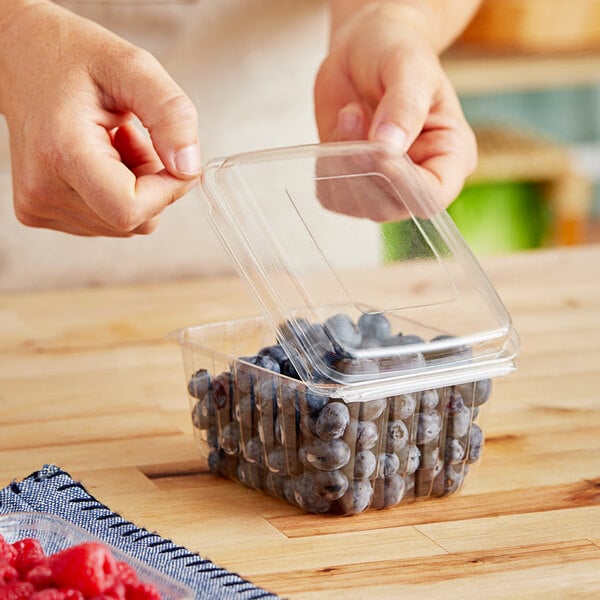 A hand putting blueberries into a D&W Fine Pack plastic clamshell container.