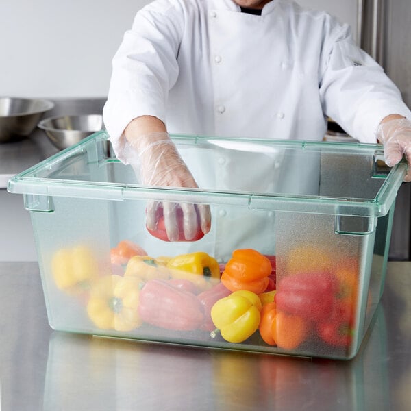 A chef in a white coat and gloves putting yellow, orange, and red bell peppers in a Carlisle green food storage box.