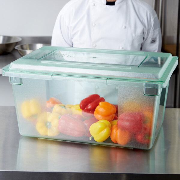 A chef standing behind a Carlisle green food storage box full of peppers.