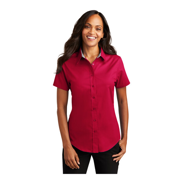 A woman wearing a red Port Authority short sleeve dress shirt with a white background.