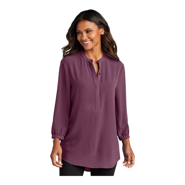 A woman wearing a purple Port Authority short sleeve blouse with a v-neck.