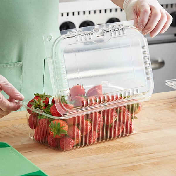 A gloved hand using a plastic clamshell container to cut strawberries.