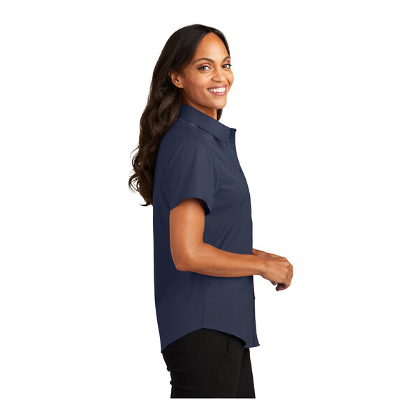 A woman wearing a Port Authority navy and light stone short sleeve dress shirt.