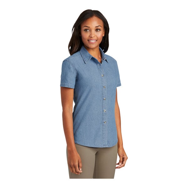 A woman wearing a Port & Company faded blue denim button-down shirt.