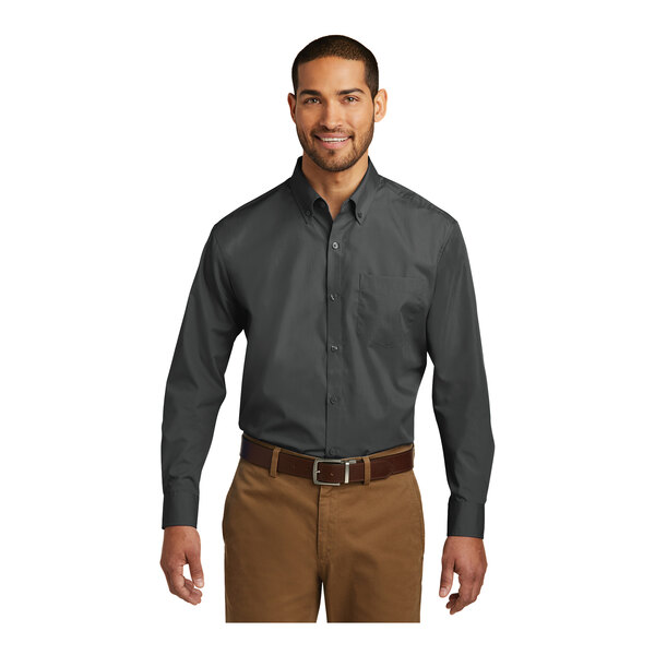 A man wearing a graphite Port Authority long sleeve poplin shirt and brown pants.