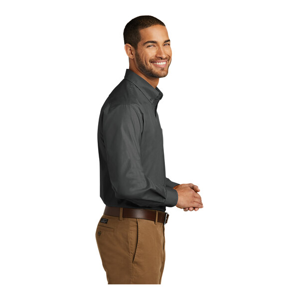 A man standing and smiling wearing a Port Authority graphite long sleeve poplin dress shirt.