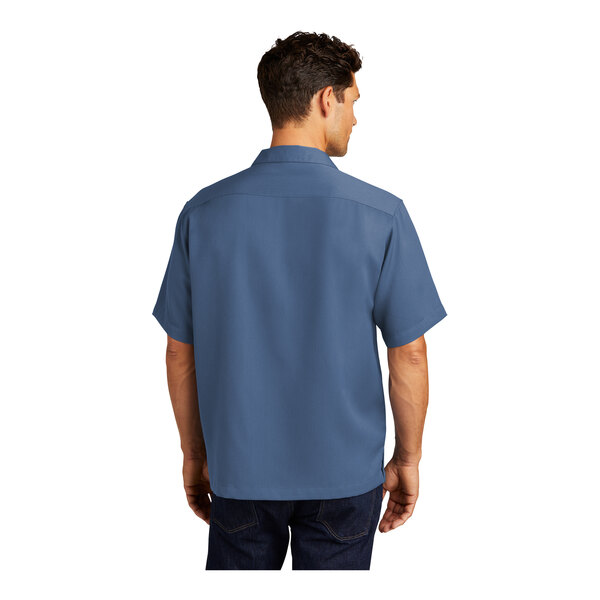 A man wearing a blue Port Authority camp shirt with stain release.