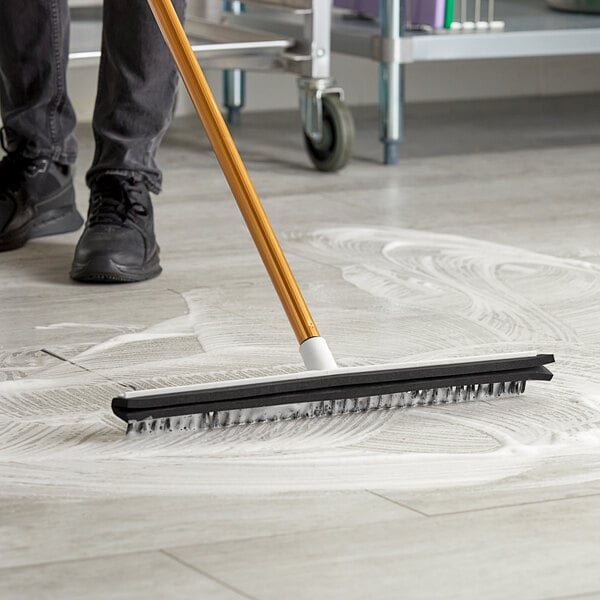 A person using an Ettore floor squeegee with a brush to clean the floor.