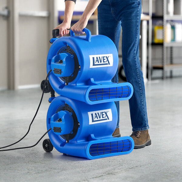 A man uses a Lavex blue air mover to dry a floor in a professional kitchen.