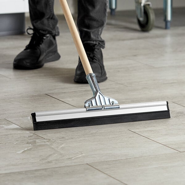 A person using an Ettore aluminum floor squeegee to clean the floor in a room.