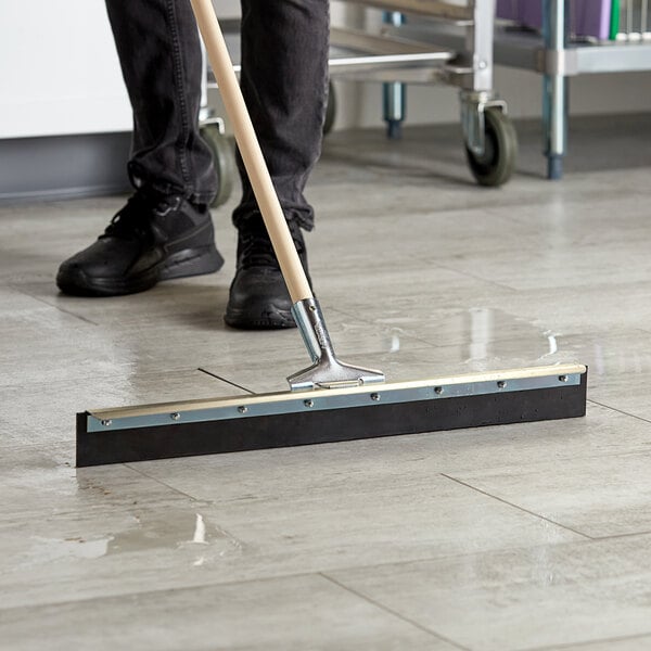 A person using an Ettore steel floor squeegee to clean a floor.