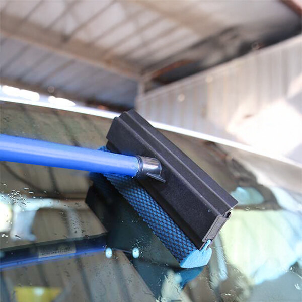 A blue-handled automotive squeegee with a black rubber blade and a blue mesh scrubber being used to clean a car windshield.