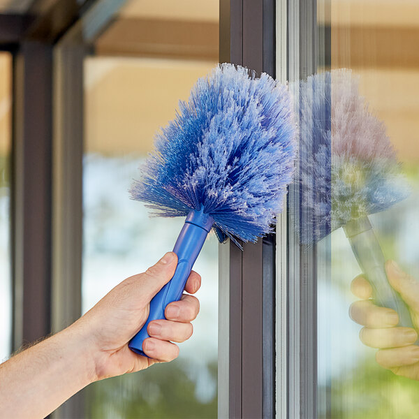 A hand holding a blue Ettore cobweb brush.