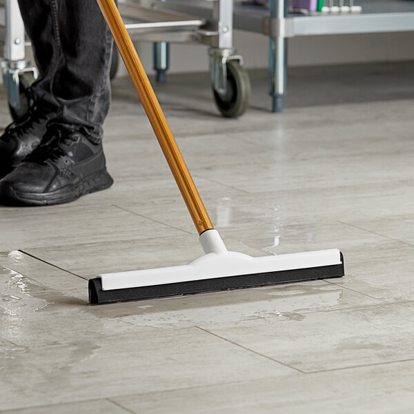 A person using an Ettore 18" floor squeegee with splash guard to clean a floor.