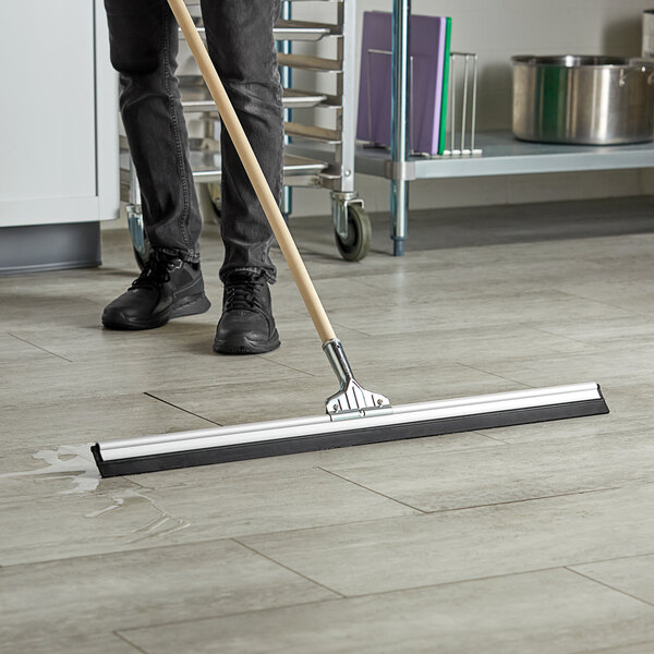 A person using an Ettore aluminum floor squeegee to clean a floor.