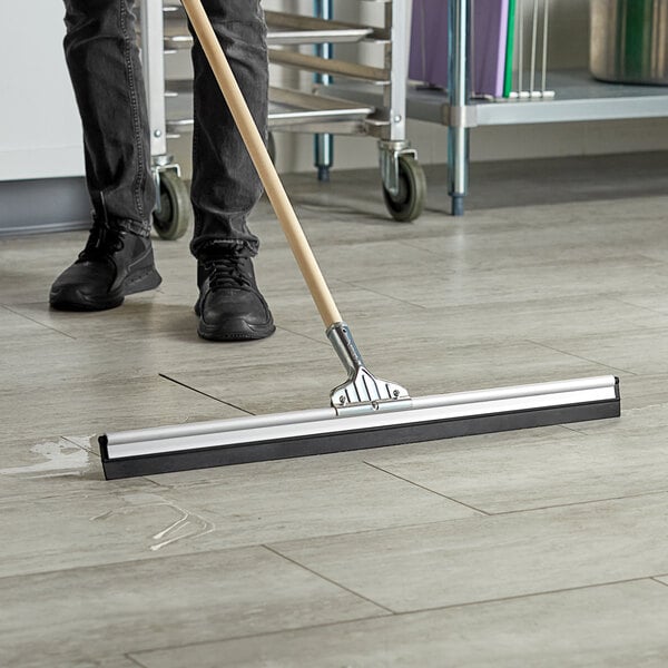 A person using an Ettore aluminum floor squeegee to clean a floor.